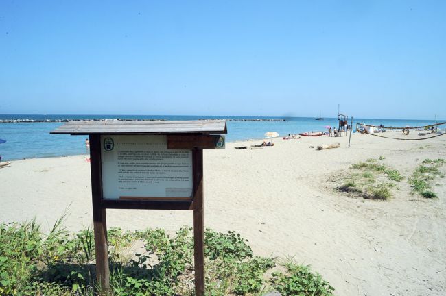 Spiaggia sabbiosa con cartello informativo e mare sullo sfondo.