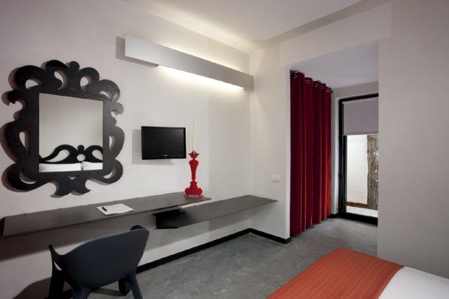 Interno di una camera da letto moderna con scrivania, specchio decorativo e tenda rossa.