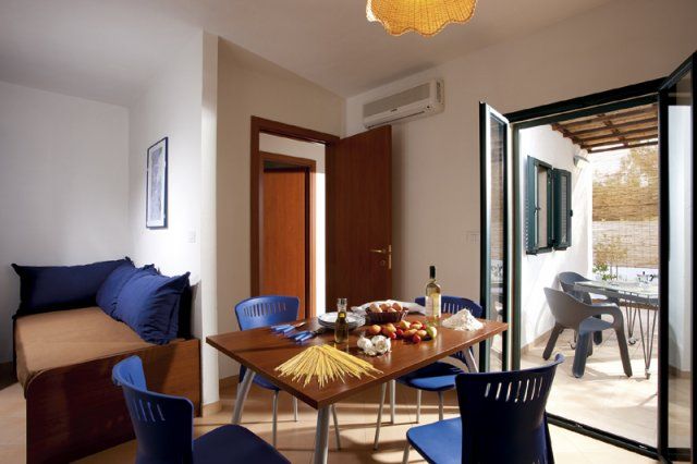 Sala da pranzo con tavolo apparecchiato, sedie blu e porte aperte su un patio esterno.