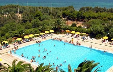 Piscina affollata con ombrelloni gialli, circondata da vegetazione verde.