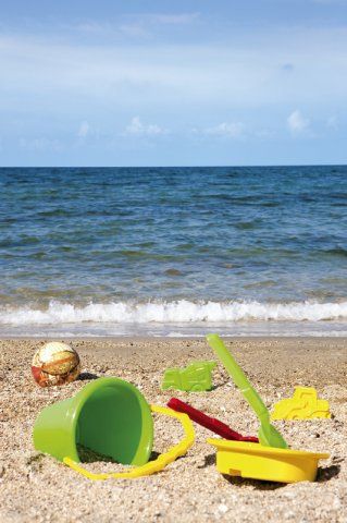 Secchiello e palette sulla sabbia di una spiaggia con il mare sullo sfondo.
