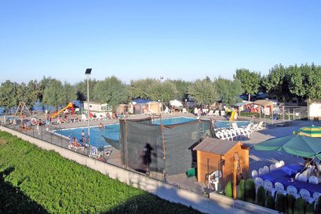 Area piscina all'aperto con sedie a sdraio e ombrelloni, circondata da alberi.
