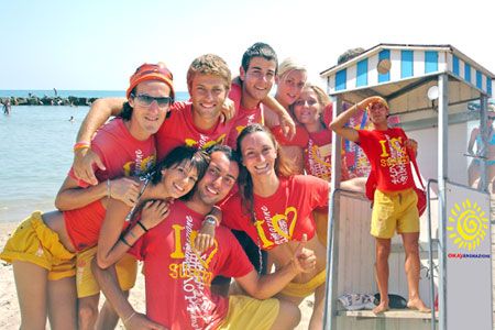 Gruppo di giovani felici in magliette rosse sulla spiaggia, vicino al mare.