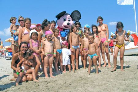 Un gruppo di bambini in spiaggia intorno a una mascotte sorridente.