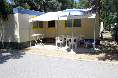Un bungalow con veranda, sedie e tavolo all'aperto su un vialetto.
