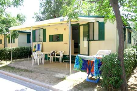 Una casa mobile con veranda coperta, sedie e tavolo all'aperto, circondata da alberi.