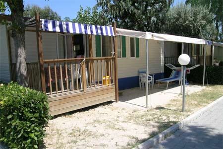 Una casa mobile con veranda in legno e tenda a righe blu e bianche, con sedie a sdraio.