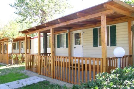 Una casa mobile con veranda coperta in legno, circondata da vegetazione.
