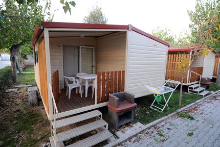 Una casetta mobile con veranda, tavolo, sedie e piccolo barbecue.