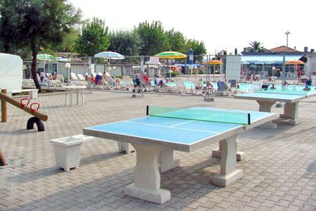 Area con tavoli da ping pong, ombrelloni e persone sedute.