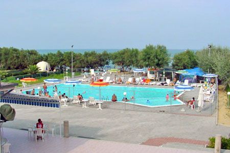 Piscina all'aperto con ombrelloni, sedie a sdraio e vista sul mare.