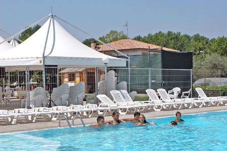 Persone nuotano in una piscina vicino a un'area con sdraio e una tenda bianca.