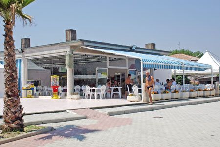Ristorante all'aperto con sedie bianche e tettoia a strisce blu.
