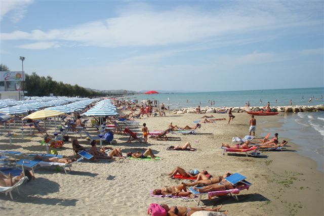 Spiaggia affollata con lettini e ombrelloni, persone che prendono il sole.