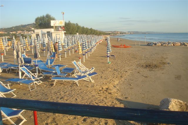 Una spiaggia con file di lettini e ombrelloni blu e bianchi lungo la costa.
