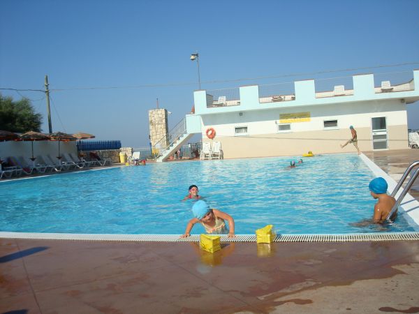 Una piscina all'aperto con bambini che giocano e un edificio sullo sfondo.