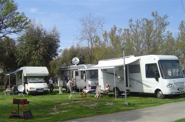 Camper parcheggiati su prato verde con persone sedute fuori a rilassarsi.