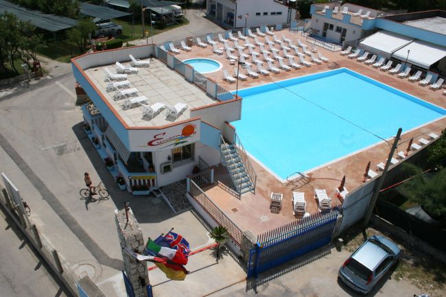 Una grande piscina all'aperto con lettini bianchi e una struttura con terrazza, vista dall'alto.