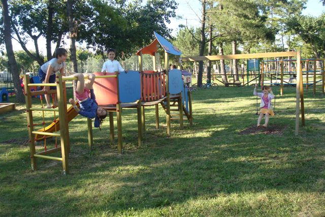 Bambini giocano in un parco con strutture di arrampicata e altalene.