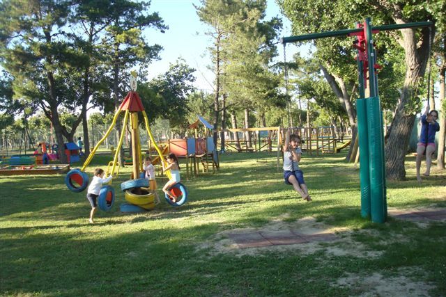 Parco giochi con bambini su una giostra e uno zip-line tra gli alberi.