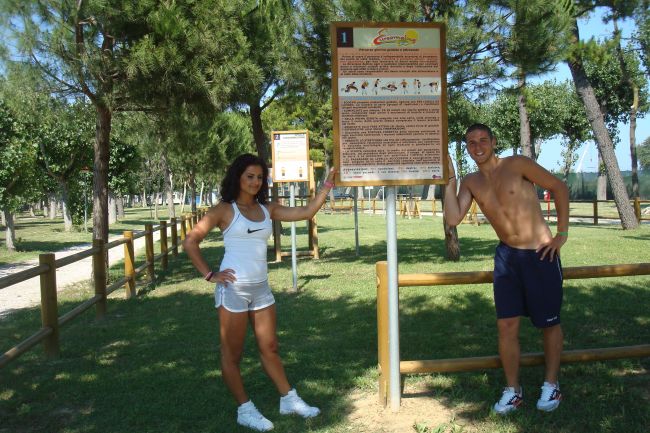 Due persone in abbigliamento sportivo posano vicino a un cartello in un parco.