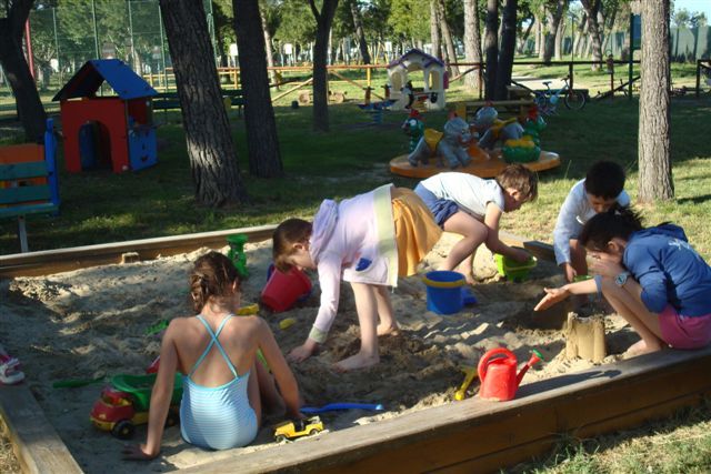 Bambini giocano con secchielli e palette in una sabbiera in un parco giochi.