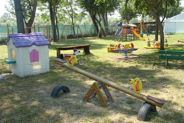 Parco giochi con altalene, scivoli e casetta giocattolo.