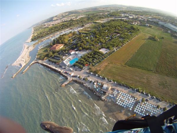 Vista aerea di una costa con spiaggia, campi, e strutture turistiche accanto al mare.