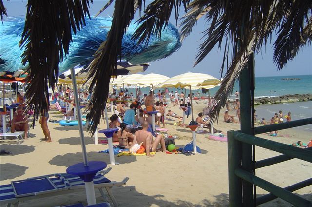 Spiaggia affollata con ombrelloni colorati e bagnanti sotto il sole.