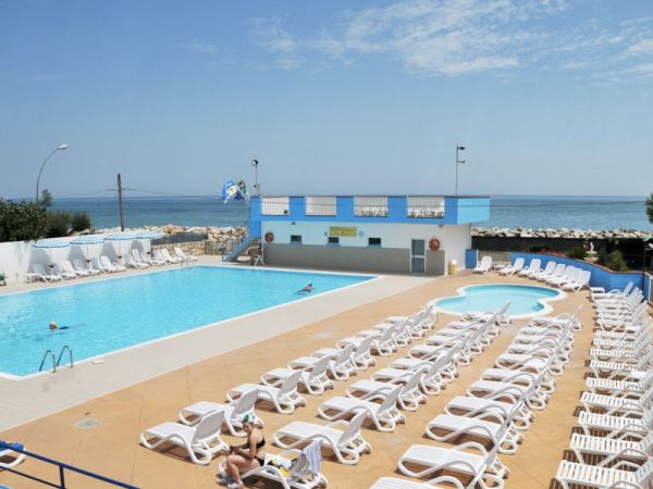 Piscina grande con lettini bianchi e vista mare.