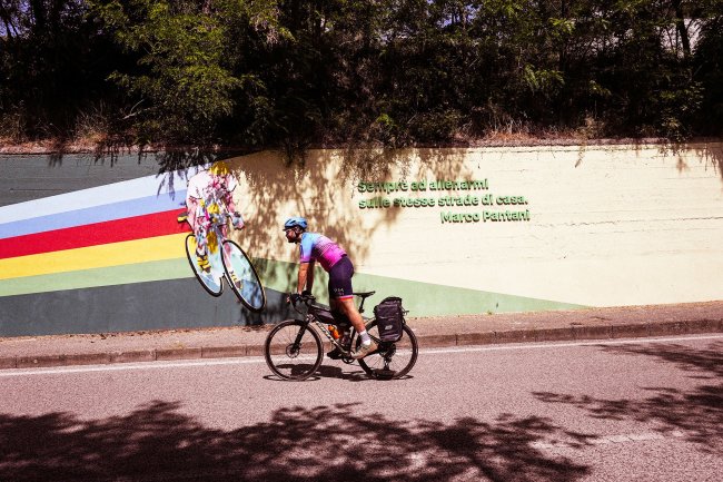 Ciclista su strada accanto a un murale colorato.