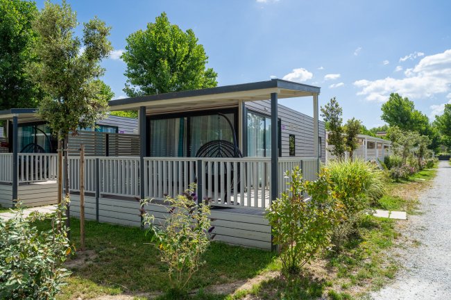 Una piccola casa prefabbricata con veranda in un campeggio verde.
