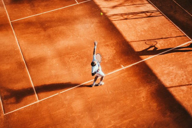 Giocatore di tennis serve su campo in terra rossa.