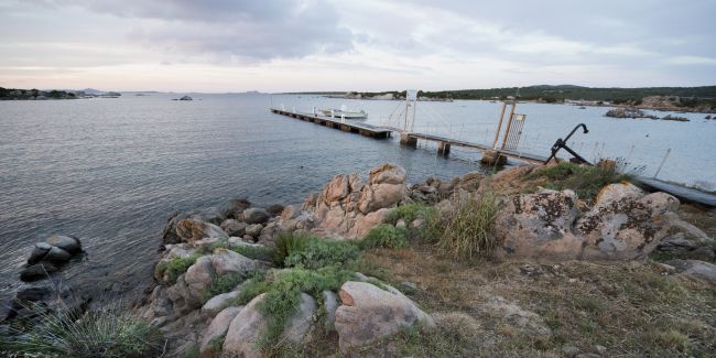 Un piccolo molo su un mare calmo con rocce in primo piano.