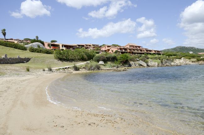Spiaggia con mare calmo e villette sullo sfondo.