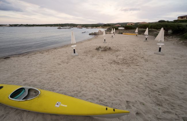 Spiaggia sabbiosa con kayak giallo e ombrelloni chiusi.