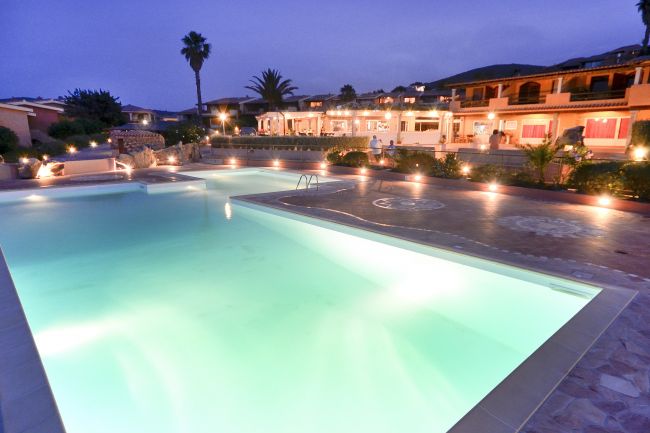Piscina illuminata di notte con edifici sullo sfondo.