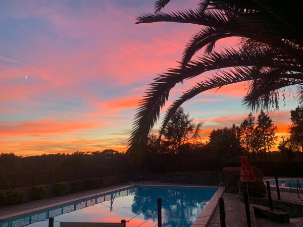 Piscina al tramonto con cielo arancione e palme.