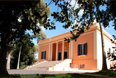 Un edificio arancione con colonne, situato tra gli alberi, sotto un cielo blu.
