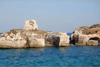 Un'antica torre diroccata su una scogliera circondata dal mare azzurro.