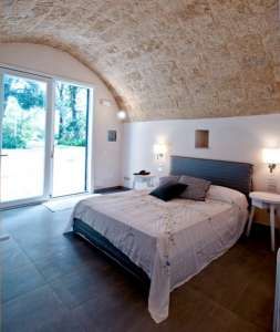 Camera con letto matrimoniale sotto un soffitto a volta, porta finestra aperta sul giardino.