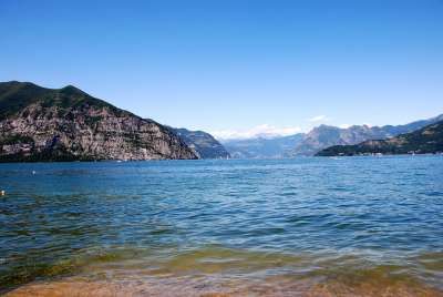 Vista di un lago con acque calme, montagne verdi e cielo sereno.