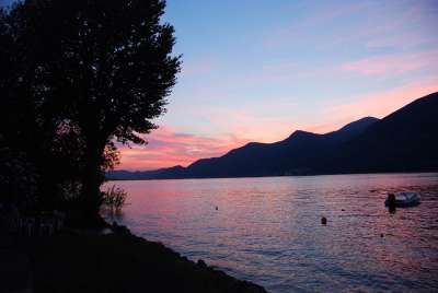 Un lago al tramonto con montagne scure e un cielo dai colori rosa e blu.