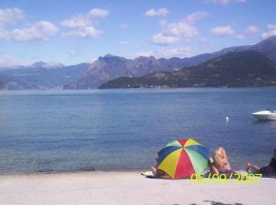 Una spiaggia con un ombrellone colorato e un lago circondato da montagne.