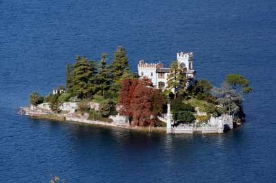 Piccola isola con un castello circondato da alberi e acqua blu.