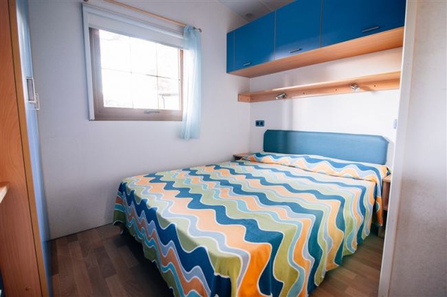 Letto matrimoniale con copriletto colorato e armadietti blu.