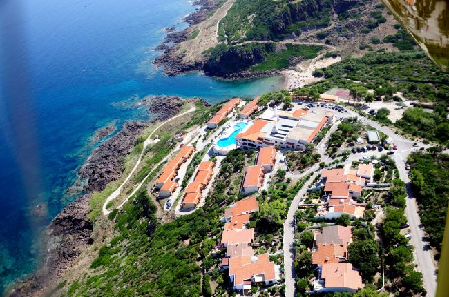 Vista aerea di un resort con tetti rossi vicino alla costa rocciosa e mare blu.