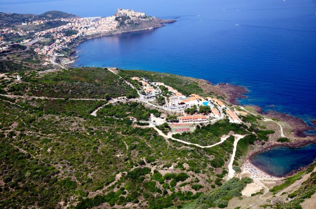 Vista aerea di una costa collinare con un villaggio e un mare blu.