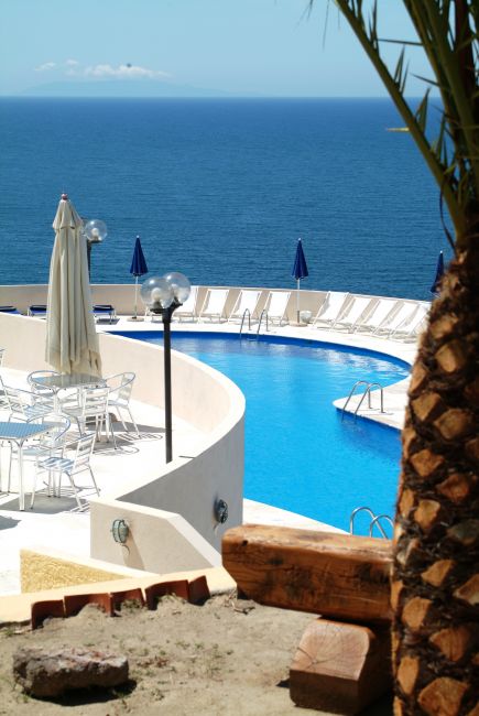 Una piscina a sfioro con vista sul mare, circondata da lettini e ombrelloni blu.
