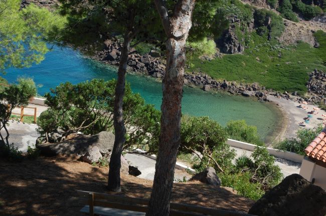 Spiaggia vista tra alberi e colline rocciose.